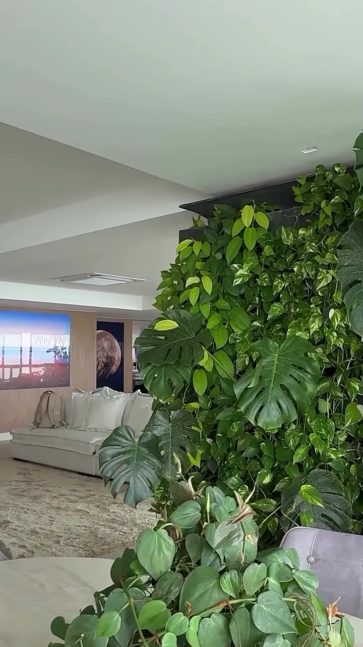 Sala ampla com jardim vertical de folhagens, mesa de pedra e sofá claro, em ambiente apresentado pela Villa Garden